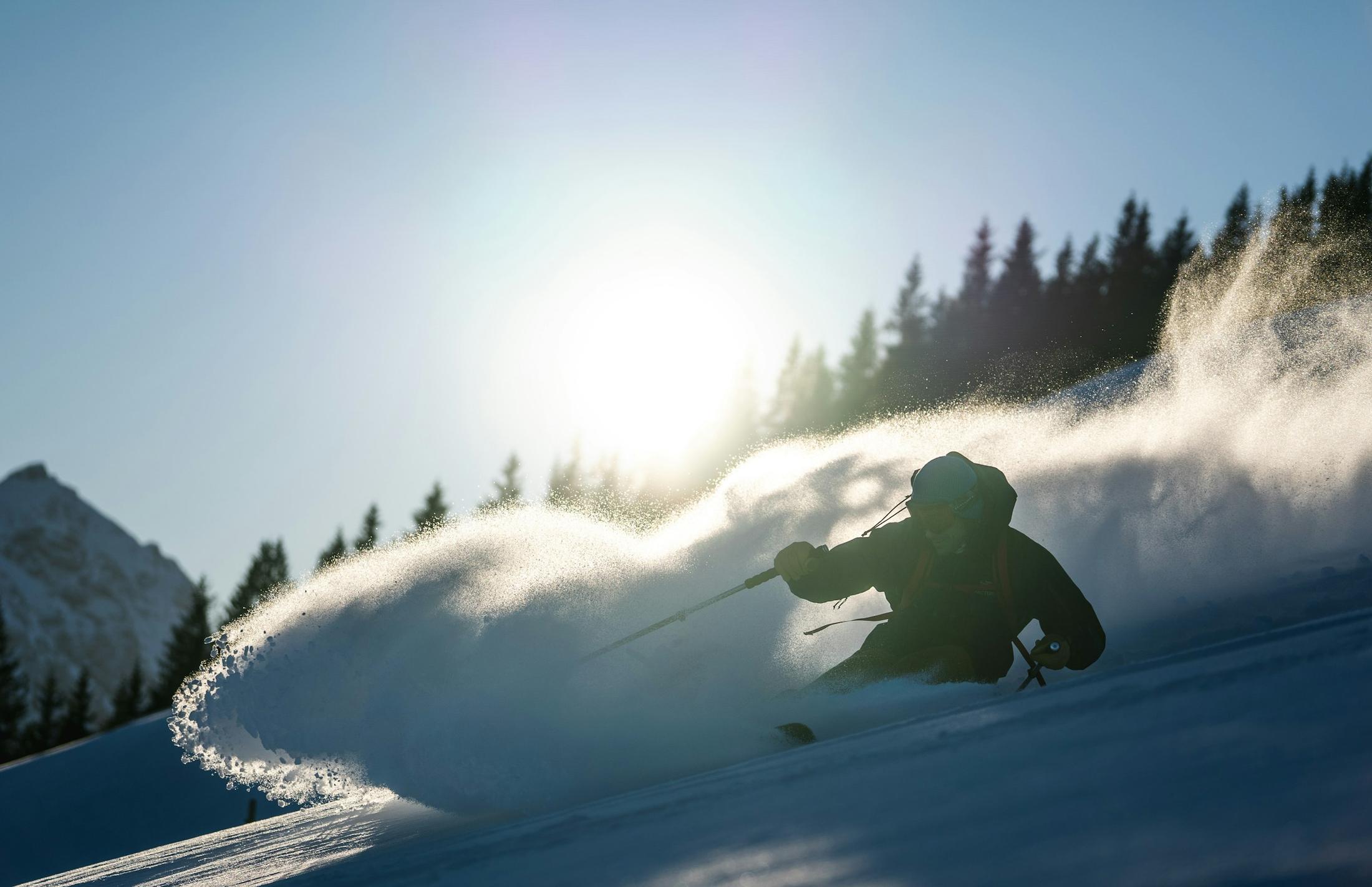 Ein Skifahrer im Gegenlicht zieht eine Pulverschnee-Fahne hinter sich her