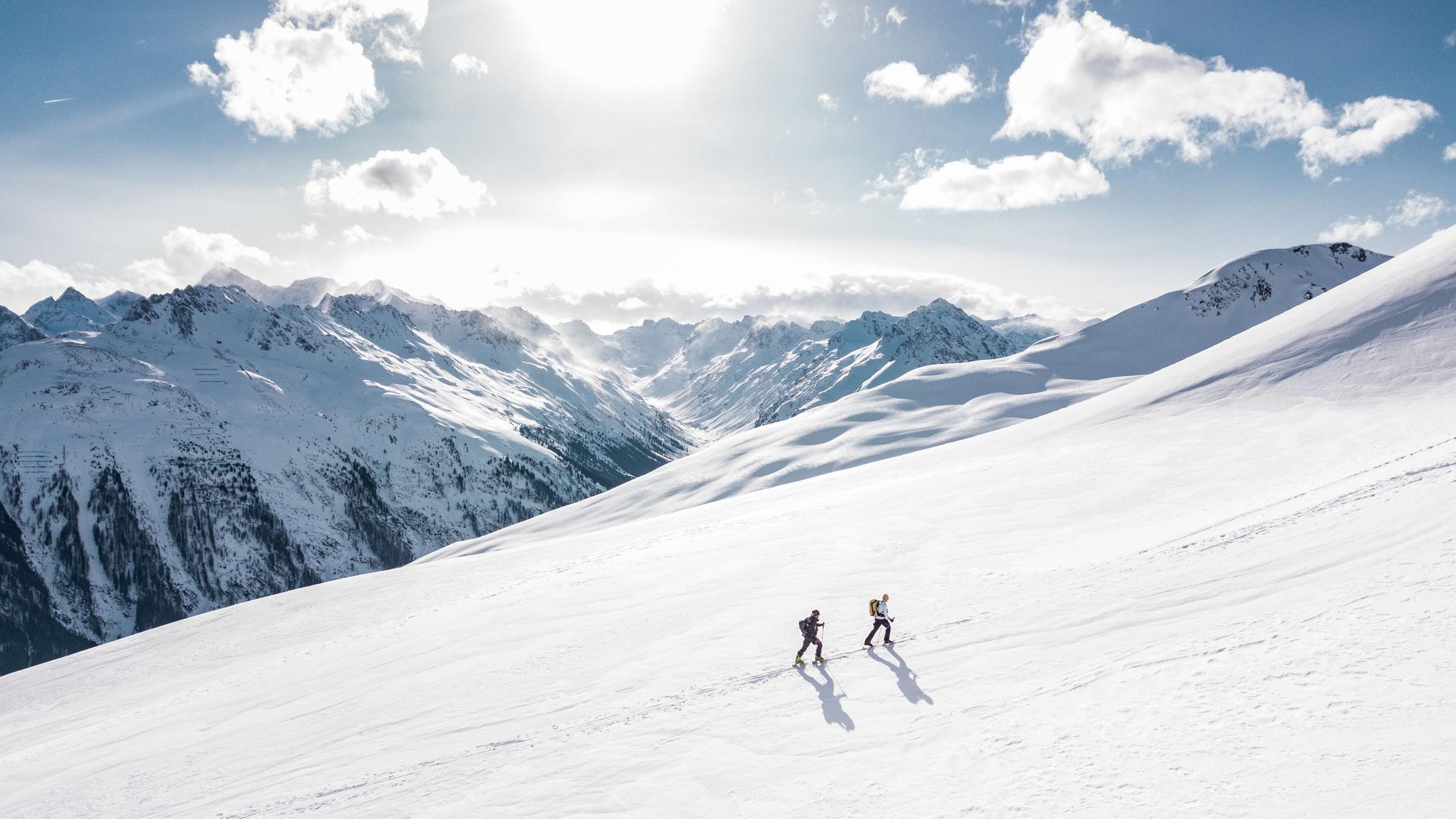 Zwei Skitourengänger ziehen ihre Spur durch einen sonnigen Neuschneehang