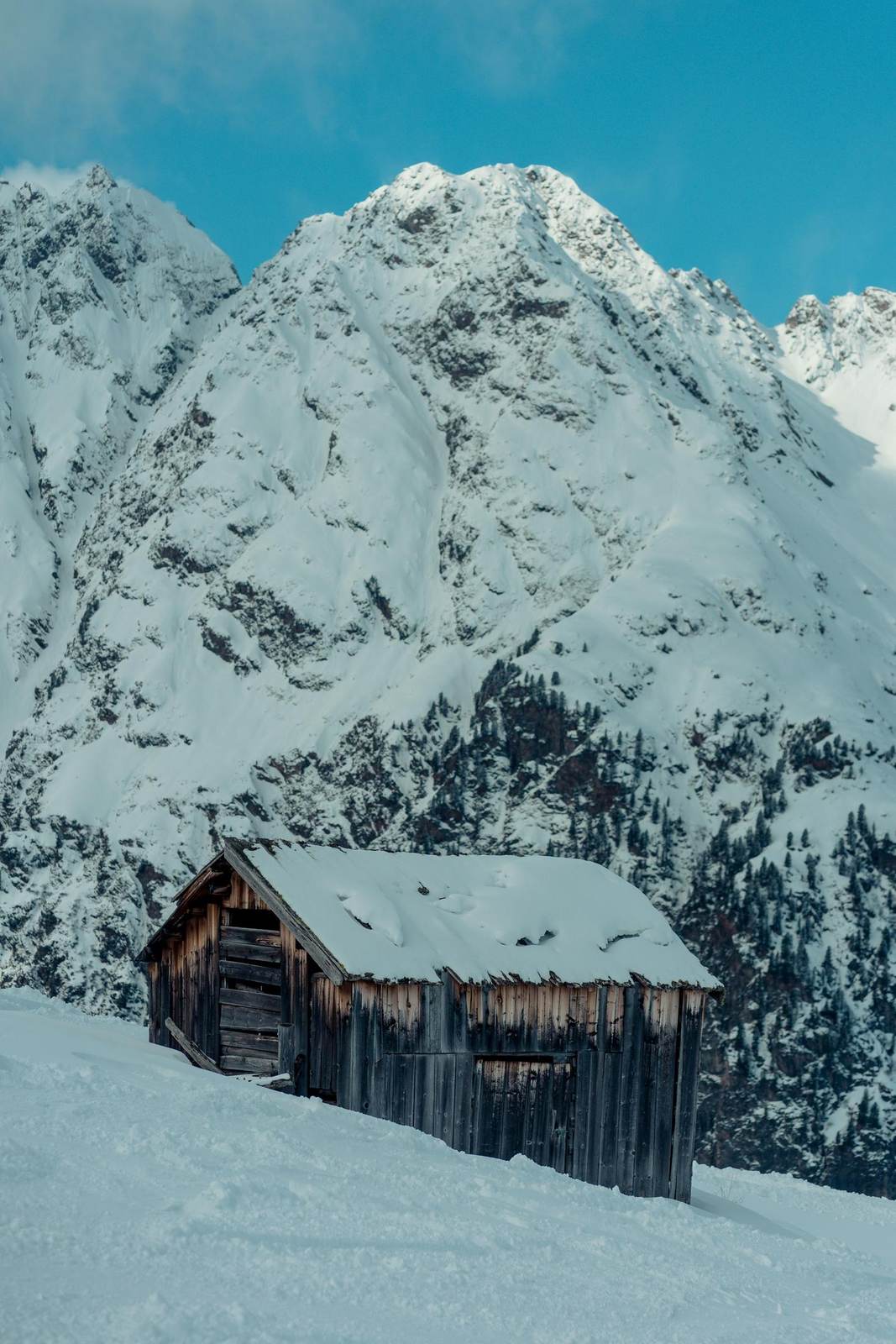 Kleine Holzhütte im Schnee unter einem Berggipfel