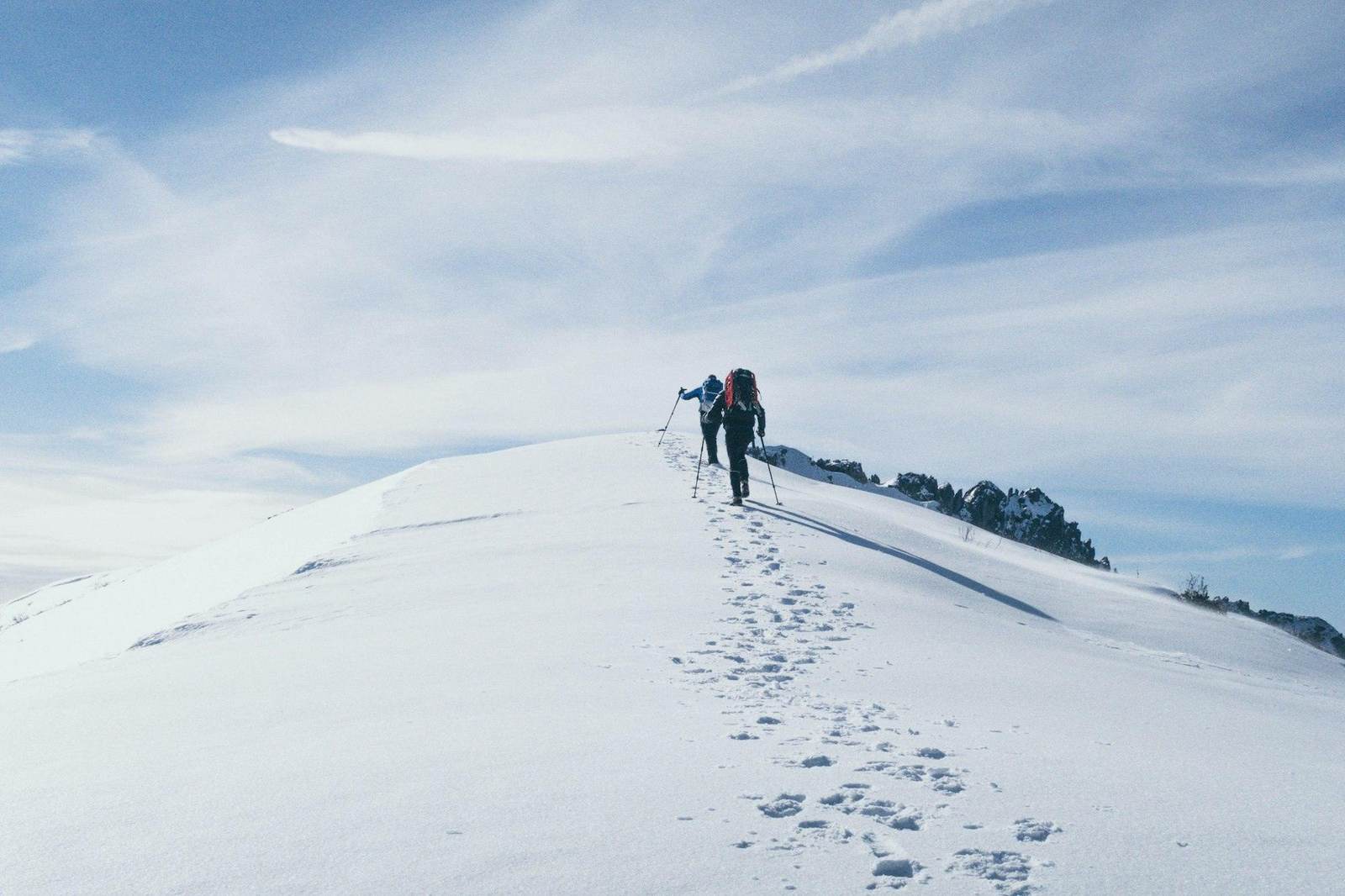 Zwei Bergsteiger gehen eine Spur über einen verschneiten Grat