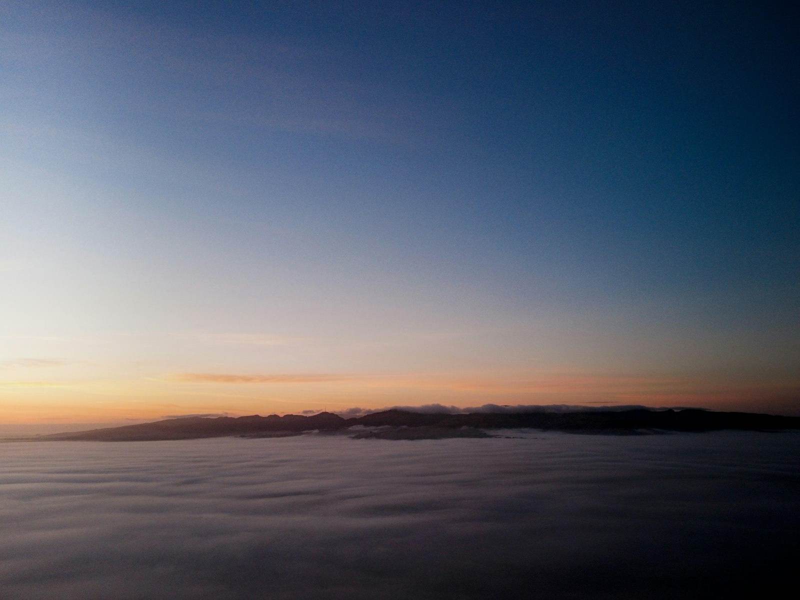 Sonnenaufgang über einem Nebelmeer, aus dem dunkle Bergrücken ragen